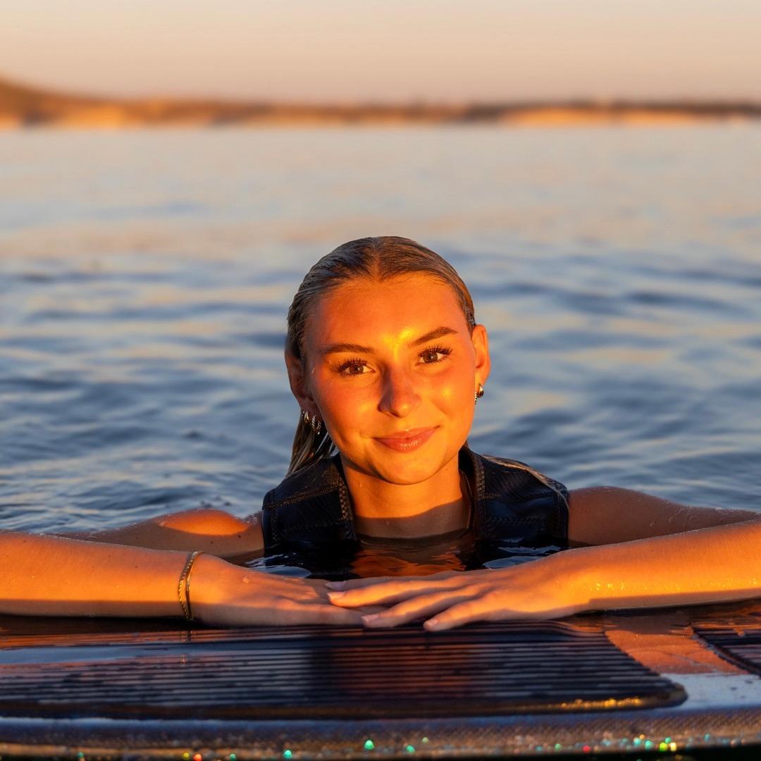 Ava Stewart with her board on the water at sunset